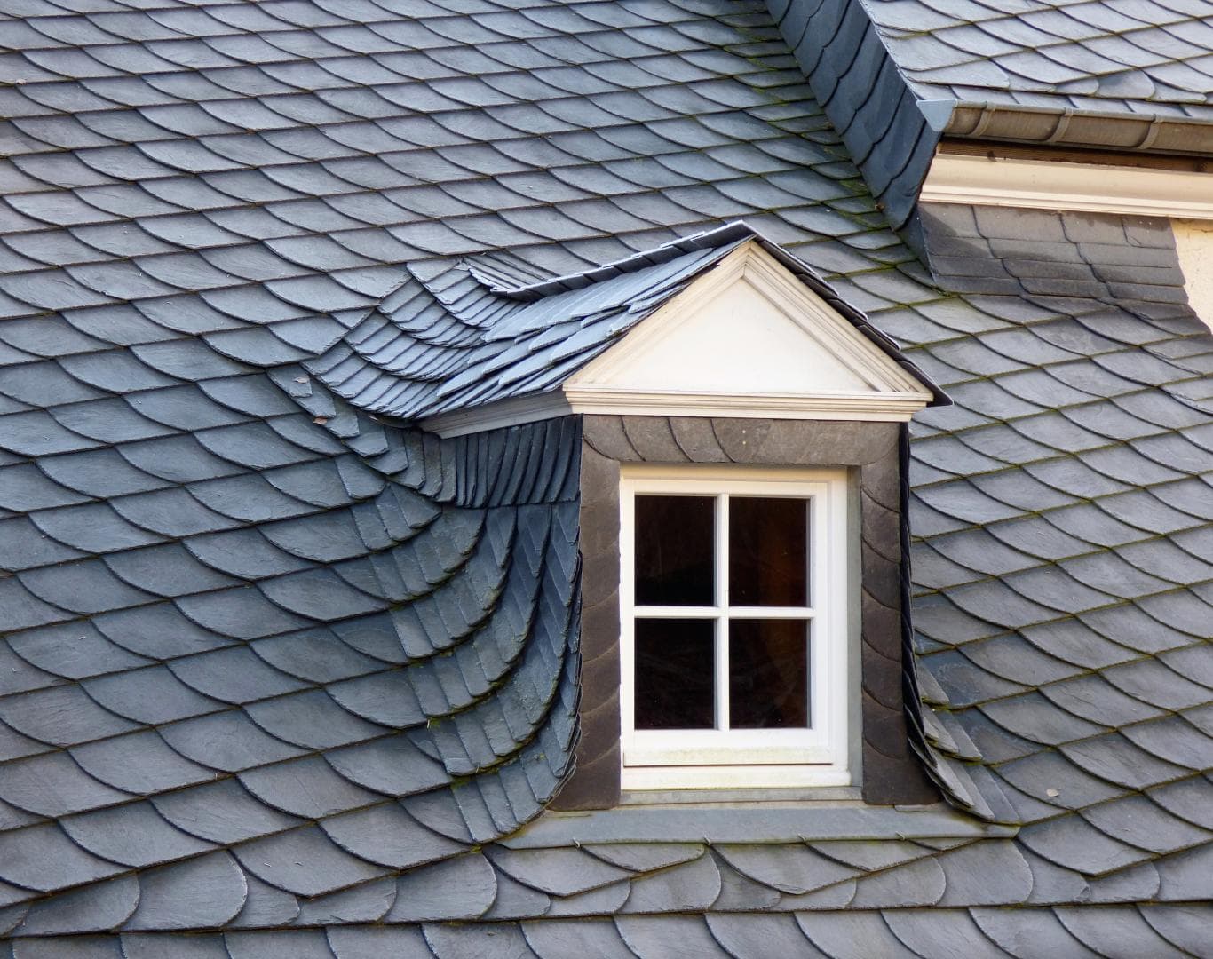 Slate roof and dormer with shaped shingle courses around the valley