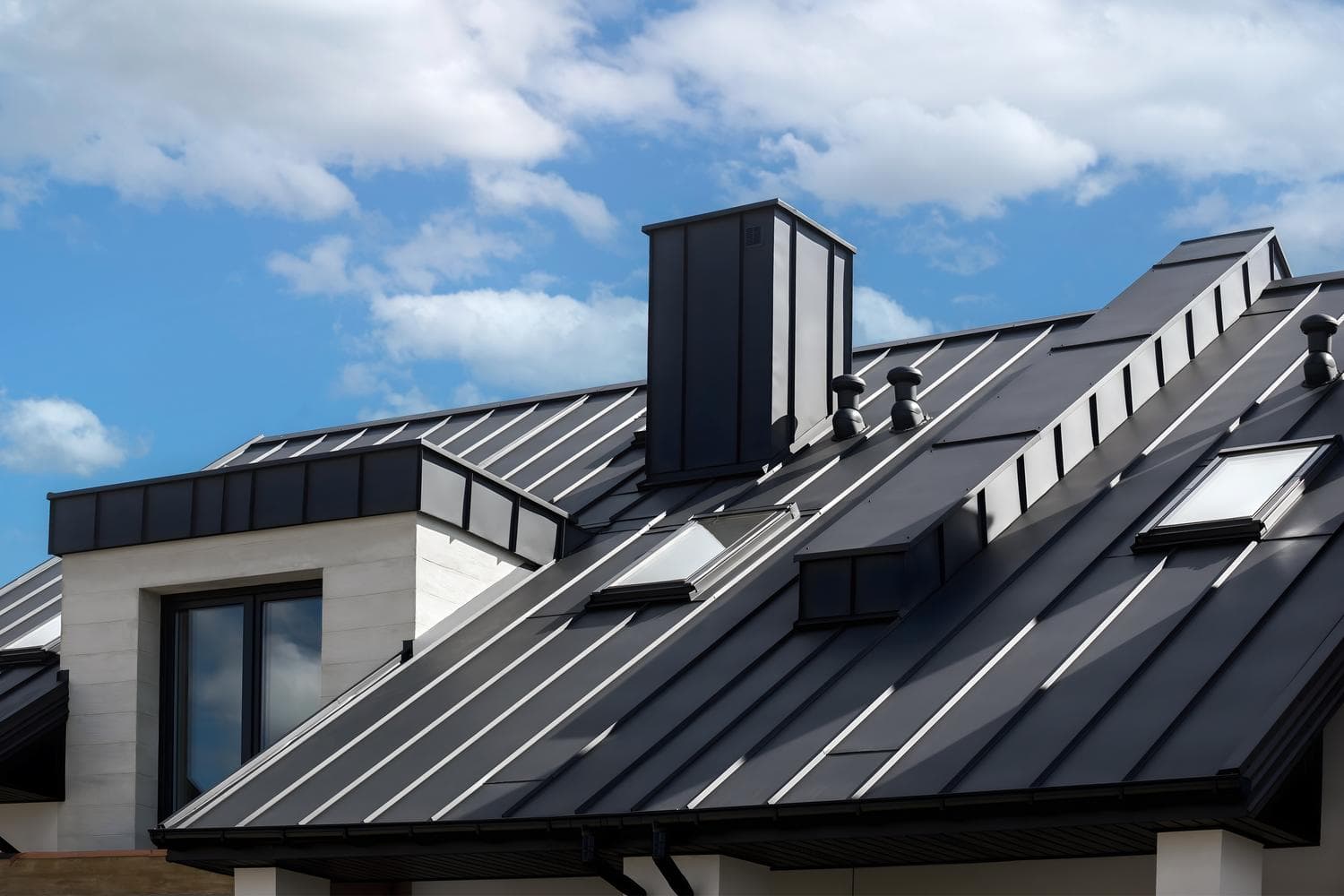 Dark standing-seam metal roof with skylights and chimney flashing